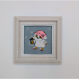 Stitched and framed embroidery artwork showing a small owl in a pink night cap holding a lantern on a soft gray background.