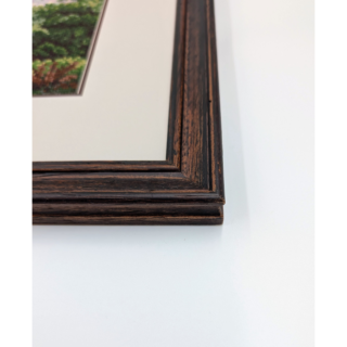 Stitched and framed embroidery artwork depicting an alpine village with a church, hillside homes, and mountains in the background.