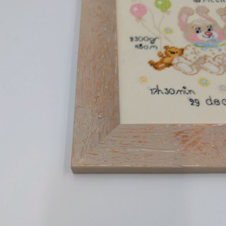 Stitched and framed embroidery artwork featuring two baby bunnies with balloons, teddy bears, and personalized birth details on a soft pastel background.