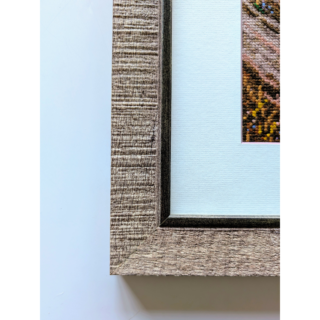 Stitched and framed embroidery artwork depicting a coastal cliff with flowering shrubs, a windswept tree, and calm sea under a pastel sky.