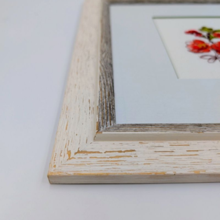 Stitched and framed embroidery artwork featuring a delicate branch of red blossoms with green leaves on a light background.