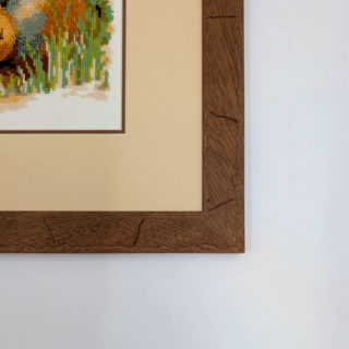 Framed stitched artwork depicting two desert foxes resting among rocks and shrubs in a warm, natural landscape.