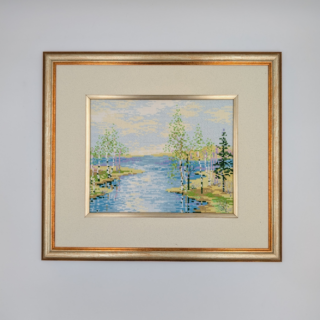 Framed stitched artwork depicting a calm river flowing between grassy banks and slender trees under a soft, clouded sky.
