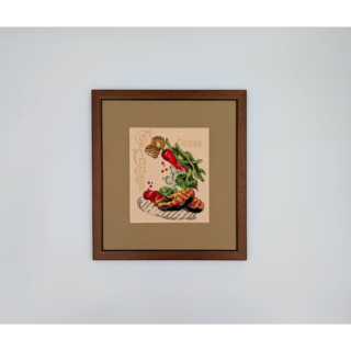 Stitched and framed embroidery artwork depicting a plated dinner with grilled meat and fresh vegetables arranged playfully.