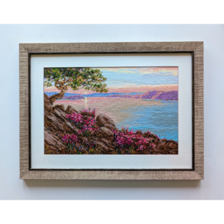 Stitched and framed embroidery artwork depicting a coastal cliff with flowering shrubs, a windswept tree, and calm sea under a pastel sky.