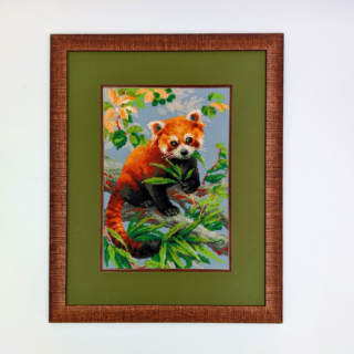 Framed stitched artwork depicting a red panda resting on a tree branch surrounded by green leaves against a soft blue background.