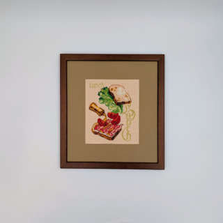 Stitched and framed embroidery artwork depicting an open sandwich with bread, lettuce, tomatoes, and cheese arranged playfully.