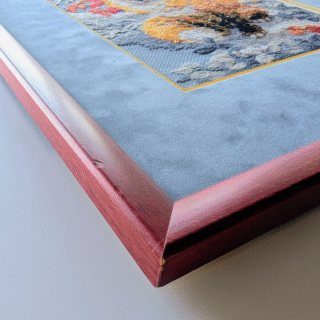 Framed cross-stitch artwork of a sitting fox surrounded by red and orange autumn leaves.