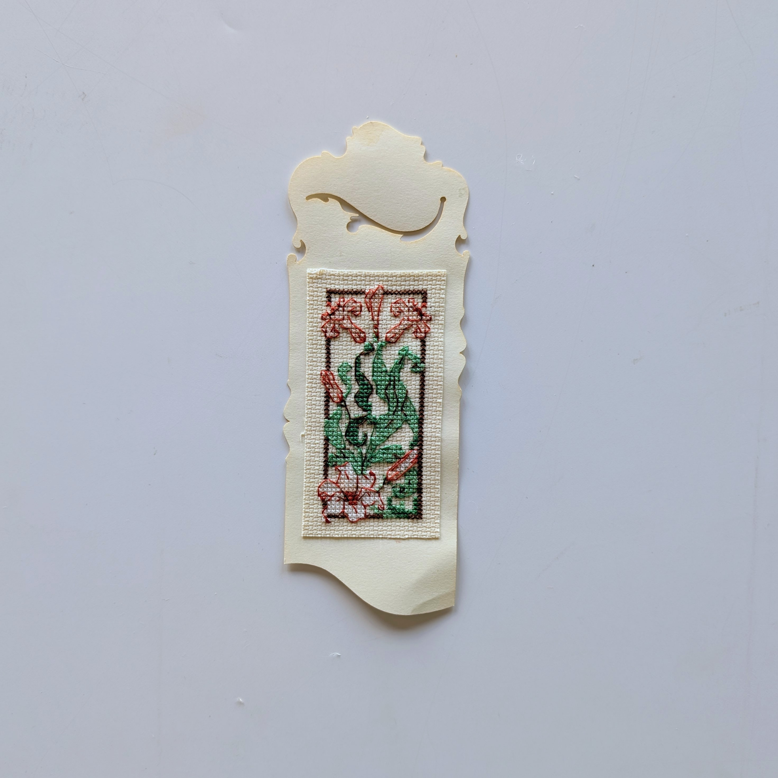 Hand-stitched floral bookmark featuring pink flowers and green leaves in an elegant decorative frame.