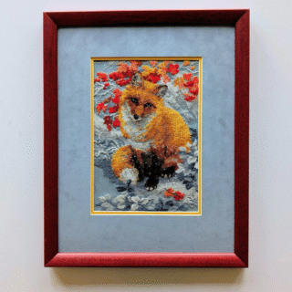 Framed cross-stitch artwork of a sitting fox surrounded by red and orange autumn leaves.