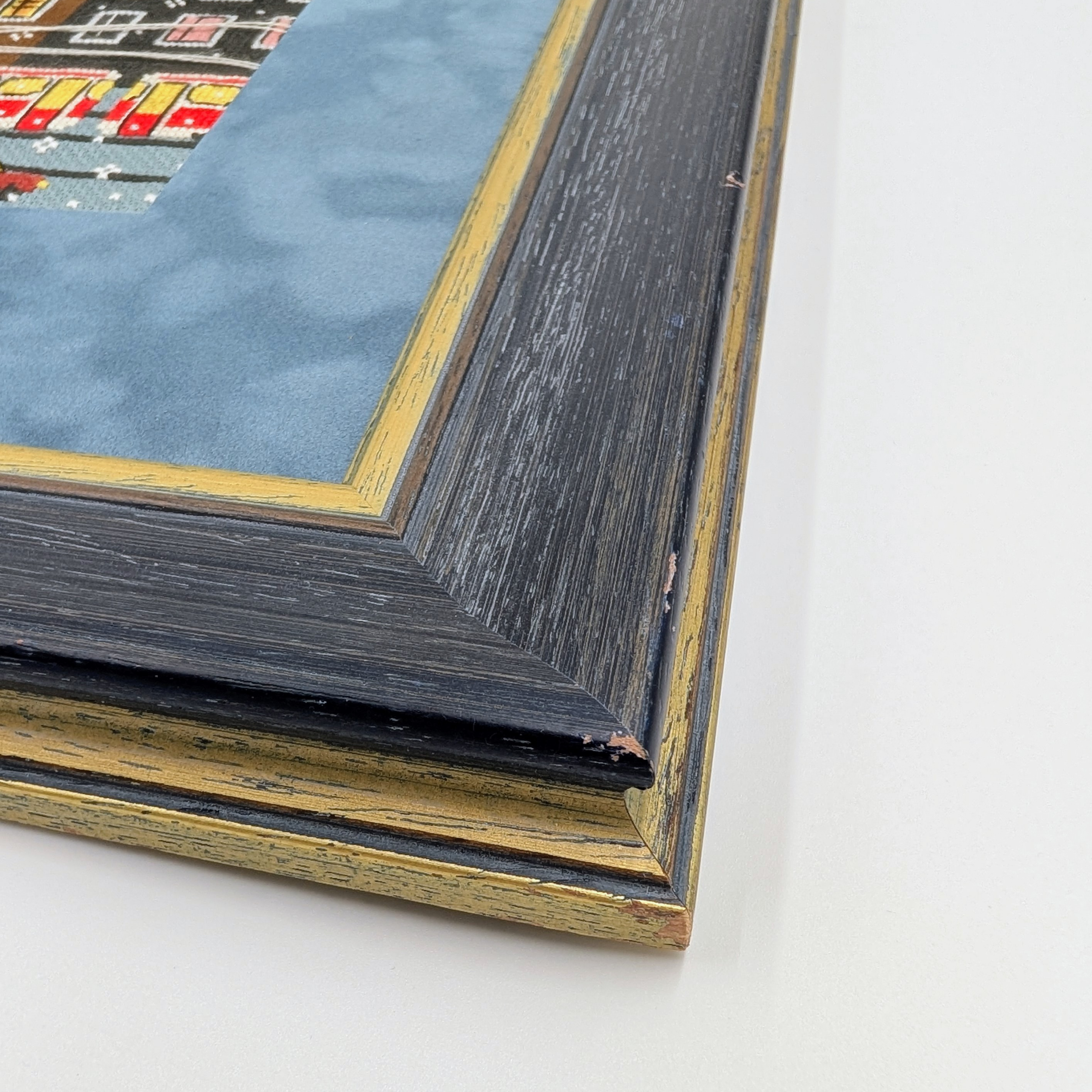 Framed cross-stitch artwork showing colorful city buildings, trams, and cars on a snowy winter day.