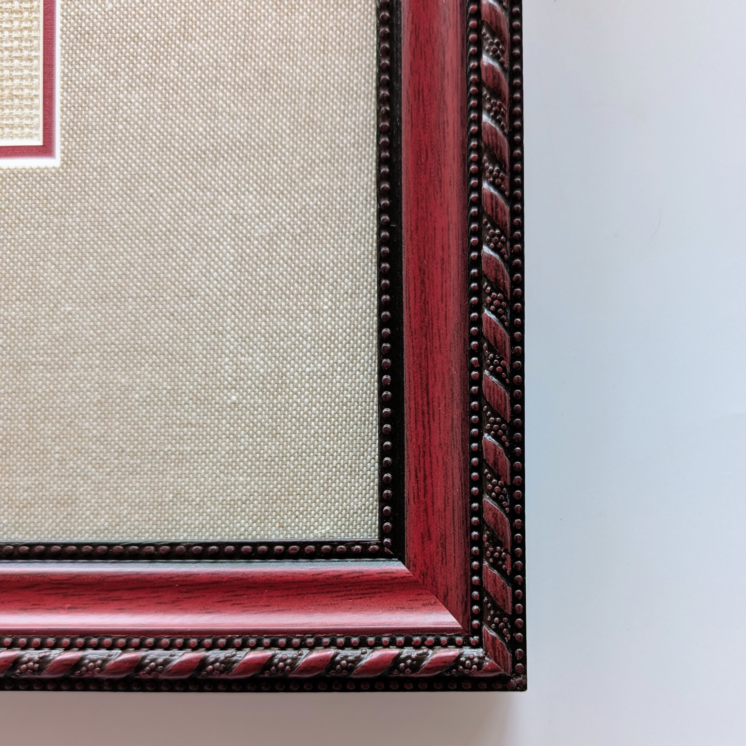 Framed cross-stitch artwork showing a bouquet of bright pink, red, and magenta dianthus flowers with green leaves.