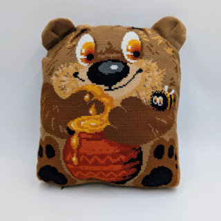 Soft stitched pillow featuring a cheerful bear holding a pot of honey with a small bee nearby.