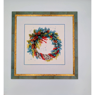 Framed embroidery artwork featuring a colorful winter wreath with pinecones, holly berries, evergreen branches, and a gray-red ribbon.