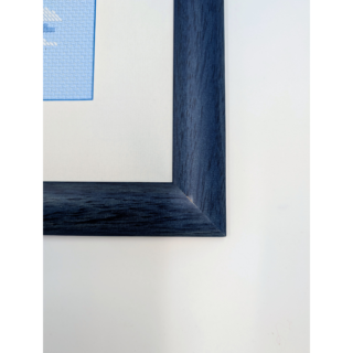 Framed and stitched cross-stitch artwork showing a husky dog standing in a snowy landscape with pine trees, wearing a blue harness.